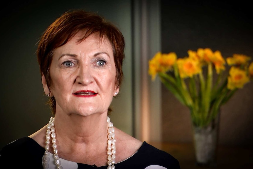 Woman with pearl necklace sitting in office with flowers in background