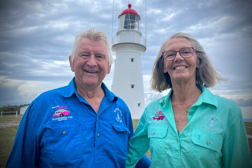 Two people with big smiles standing in front of a lighthouse on a stormy day
