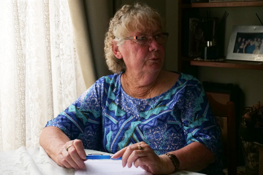 Woman looks into the darkness, holds a pen with papers underneath her hands