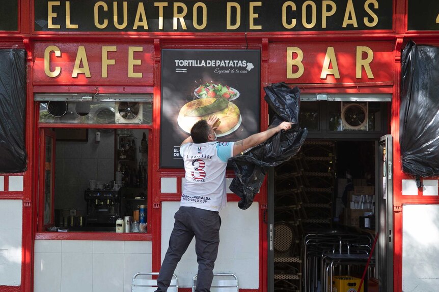 A man is taking off coverings from a bar and cafe whose exteriors are painted red.