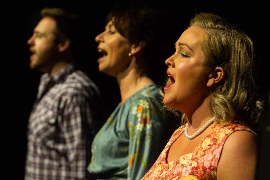 Three singers in a row on stage, all hitting a peak note.