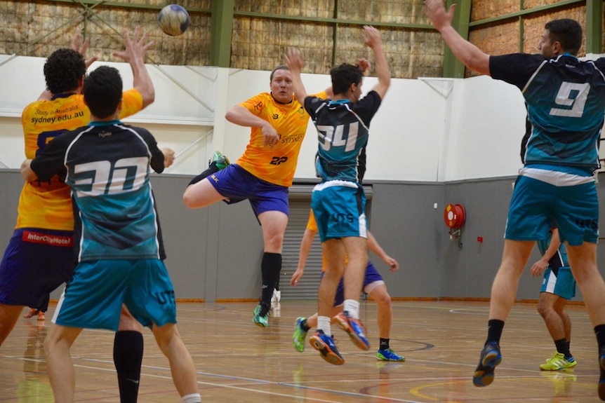 A Sydney Uni handball player jumps and throws the ball as opponents try and stop him.