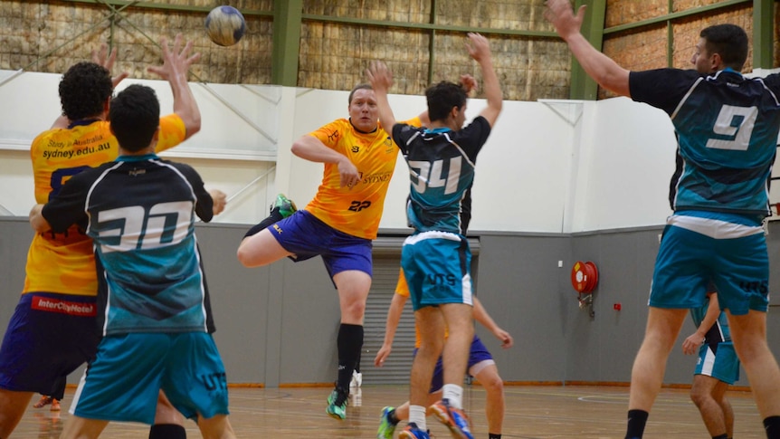 A Sydney Uni handball player jumps and throws the ball as opponents try and stop him.