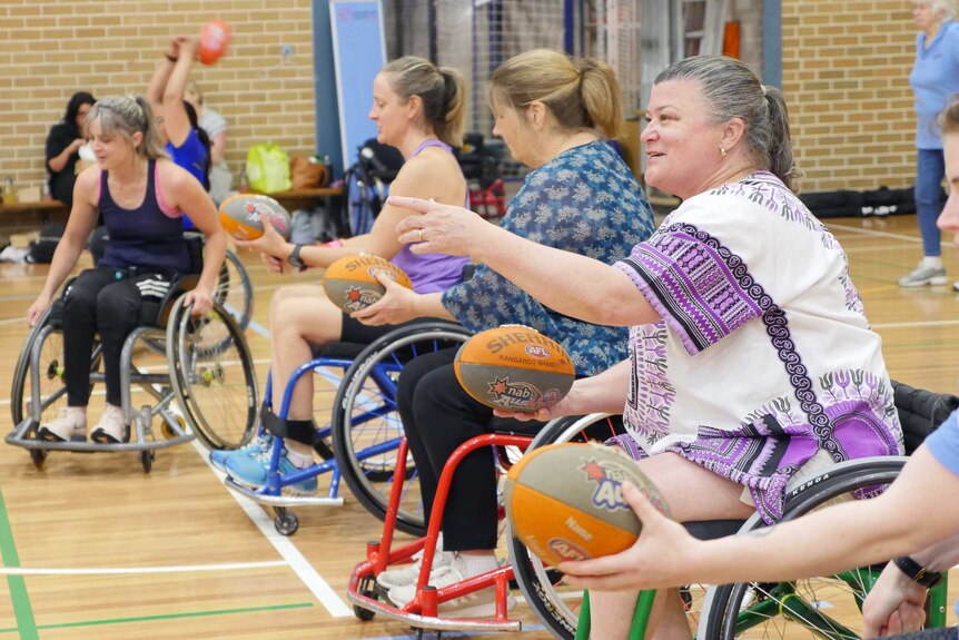 A group of women sit in wheelchairs and hold Aussie rules footballs.