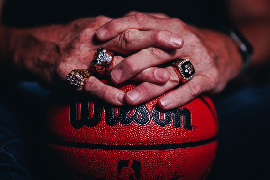 Luc Longley's hands wear his three championship rings and rest on a basketball.