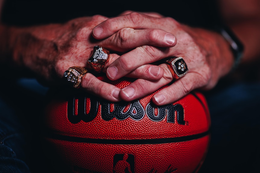 Luc Longley's hands wear his three championship rings and rest on a basketball.