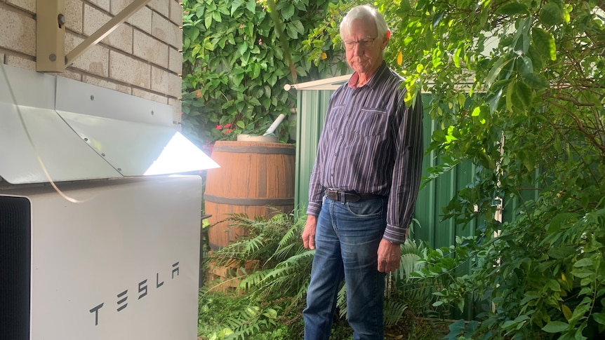 A man stands looking at a Tesla battery on the side of his home.