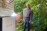 A man stands looking at a Tesla battery on the side of his home.