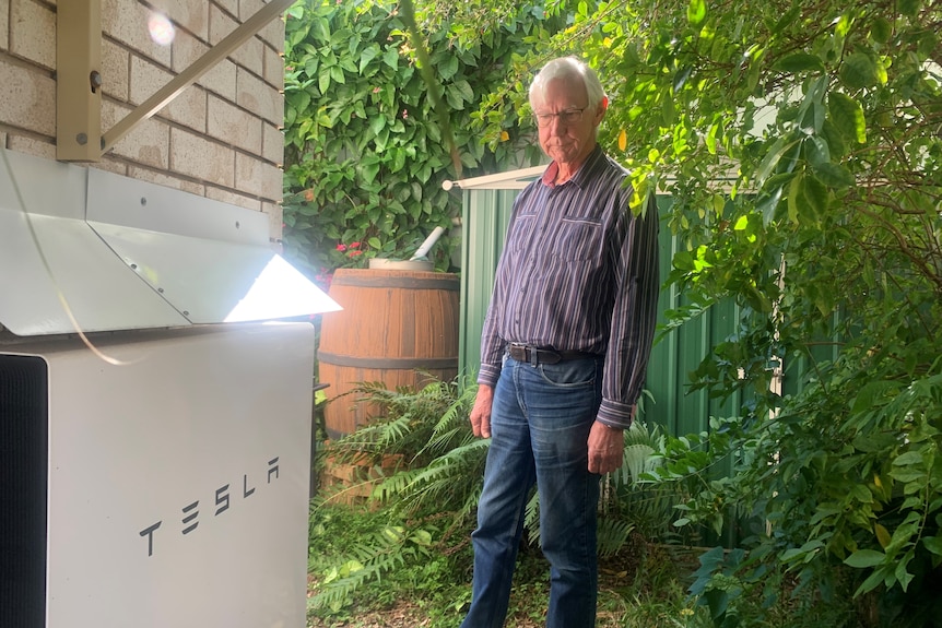 A man stands looking at a Tesla battery on the side of his home.