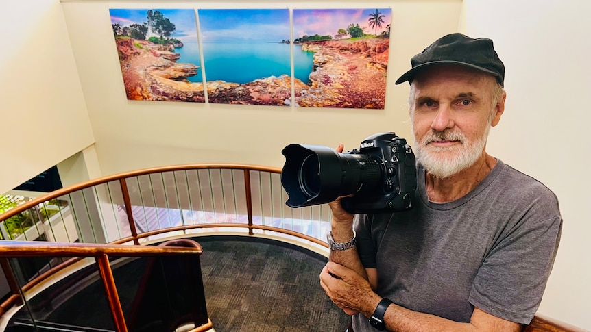 Man holds a camera in front of a large picture of the ocean