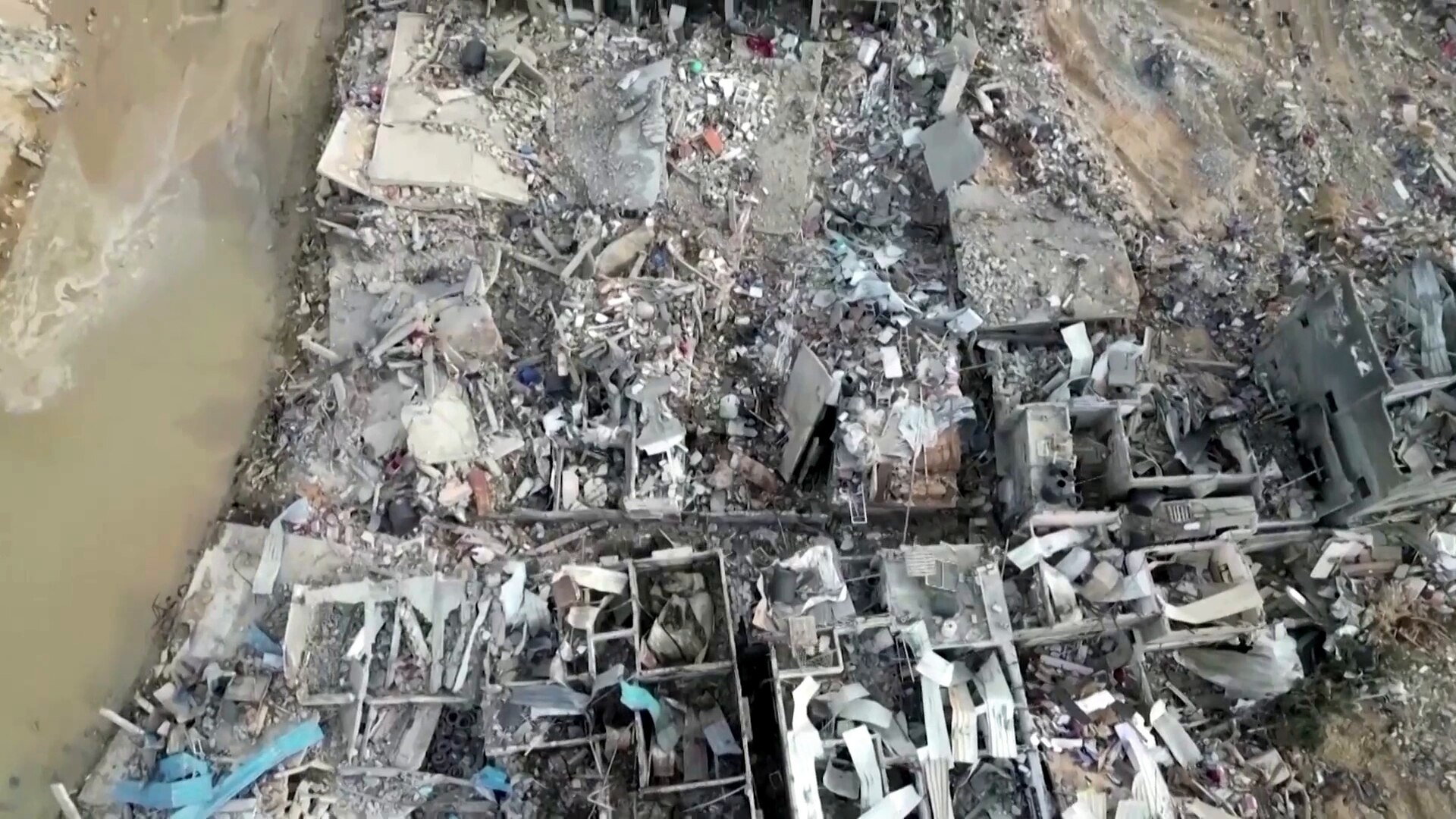 drone photo of destrroyed buildings on the edge of a murky river