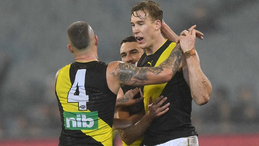 Two AFL players — one with his back to the camera — celebrate a goal in the wet at the MCG.