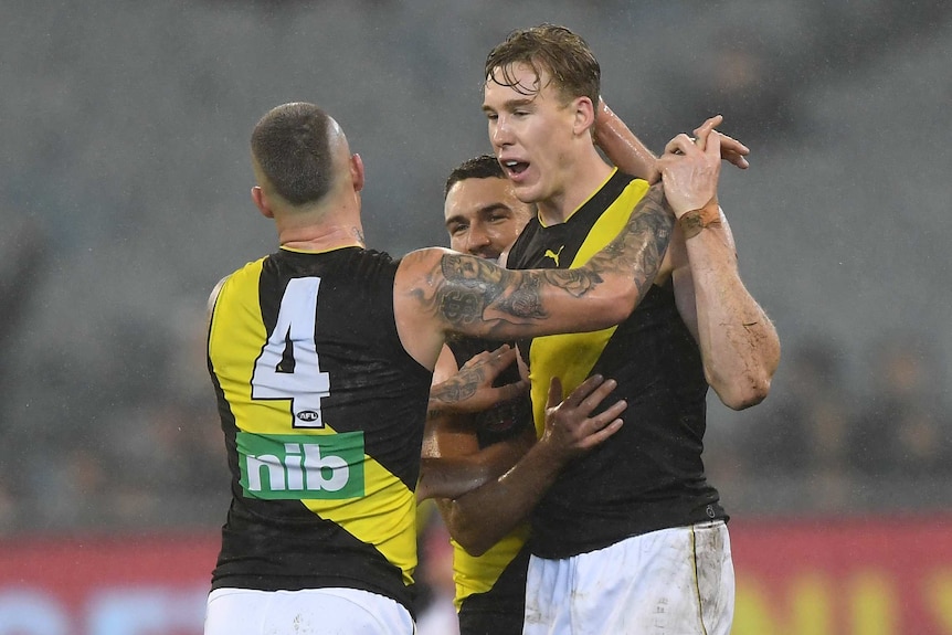 Two AFL players — one with his back to the camera — celebrate a goal in the wet at the MCG.