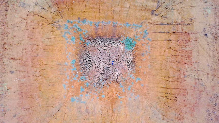 A farmer walks over a dried up dam, pictured from above.