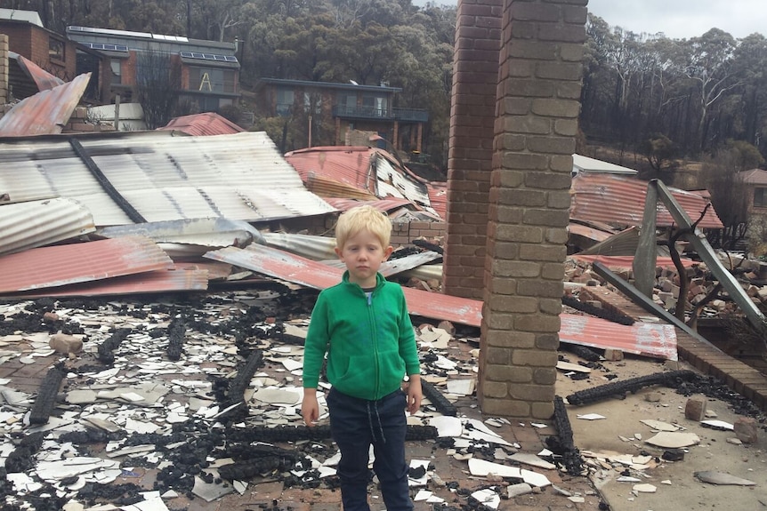 A young boy stands in the ruins of a burned-down house.