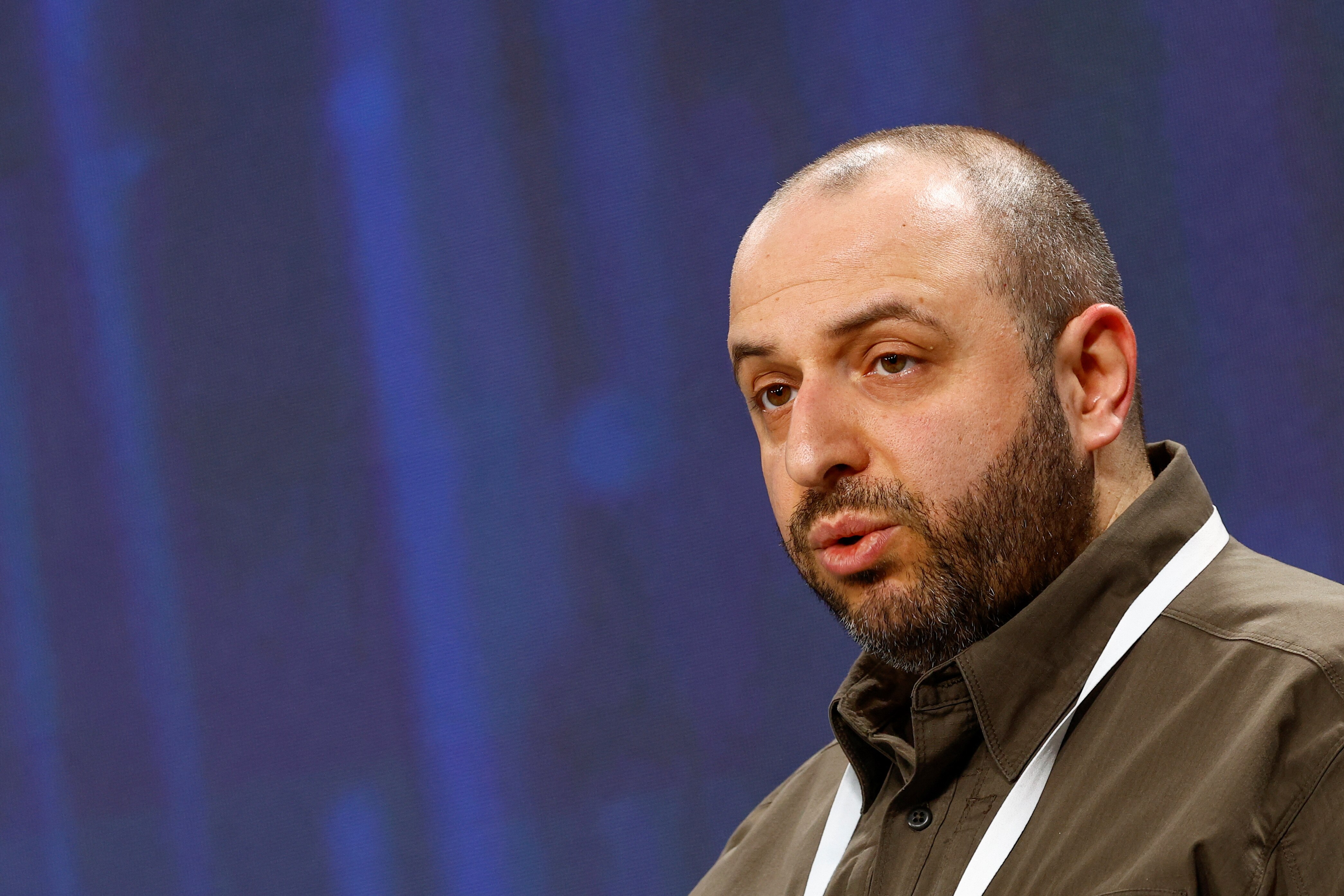 Rustem Umerov speaking in a shirt at a press conference with a blue background