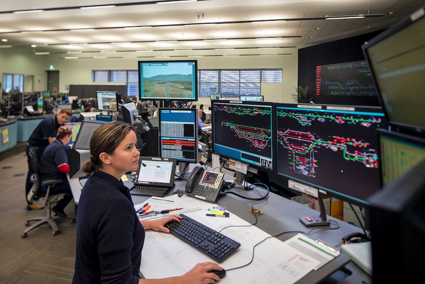 Workers in front of banks of computers and monitors remotely running operations at  Rio Tinto iron ore mines in WA