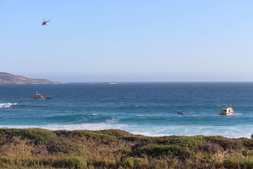 A beach pictured with a helicopter above, rescue boats in the water and jet skis.