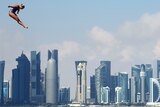 Rhiannan Iffland hovers in the air during a high dive with Doha skyscrapers visible behind her