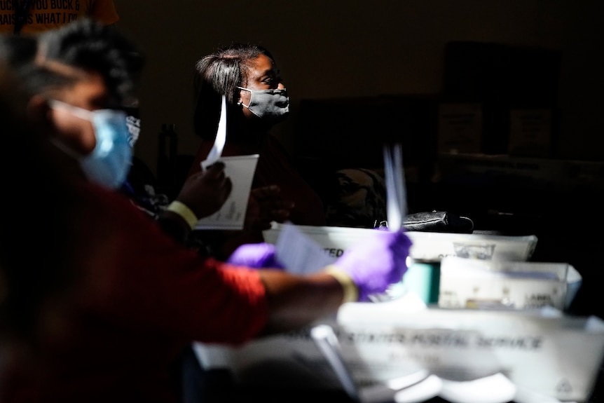 Two women sitting at tables, wearing face masks and counting votes in the US election