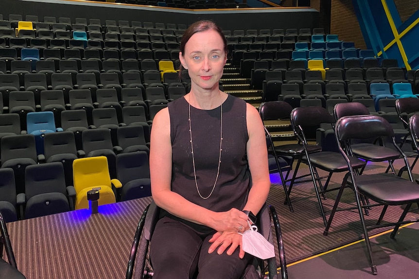 A woman wearing a black dress smiles in front of rows of empty theatre chairs