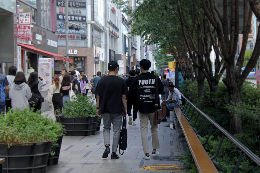 Two young men walking away on a busy street in Seoul, with one wearing a shirt that says 'Youth'.