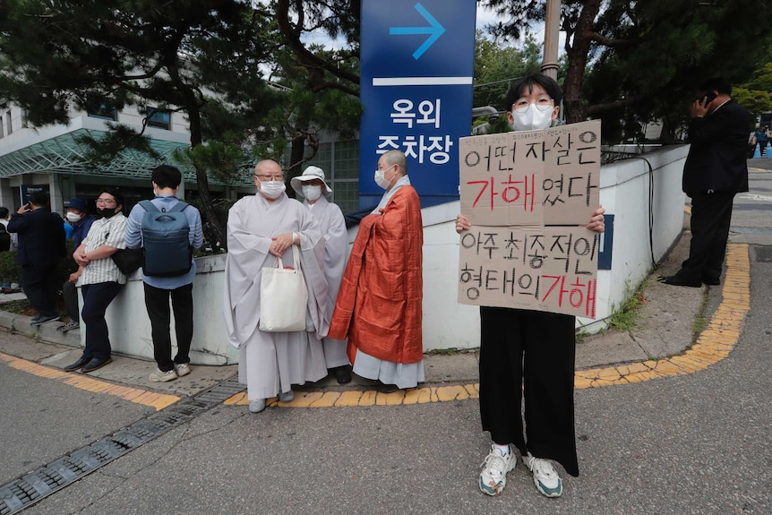 A person in a face mask holds a sign with Korean writing on it.