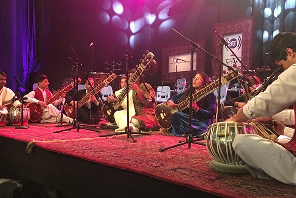 Members of ANIM sit on the floor of a stage performing traditional Afghan instruments.