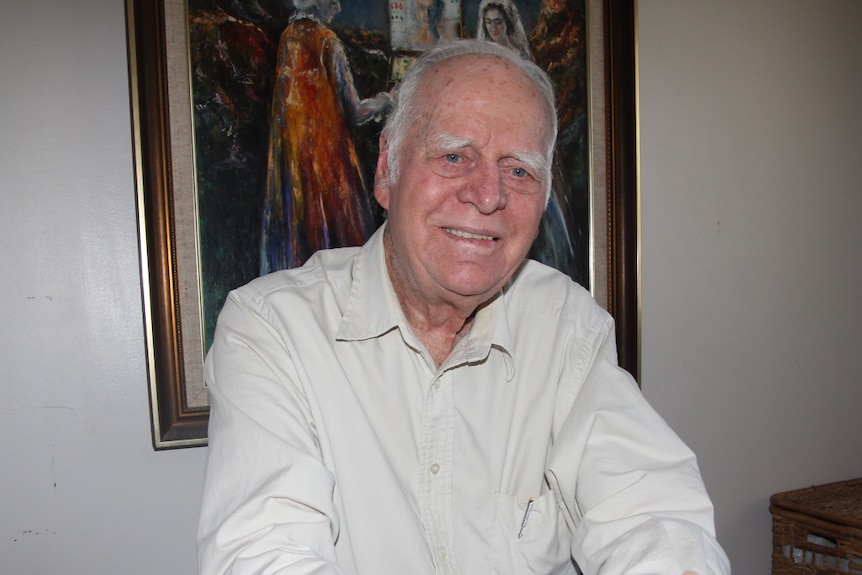 A man sits at a dining table in front of a painting