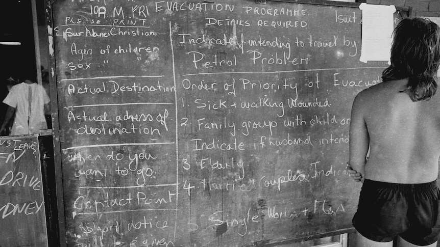 A survivor reads a blackboard showing evacuation priorities in after Cyclone Tracy struck Darwin in December 1974