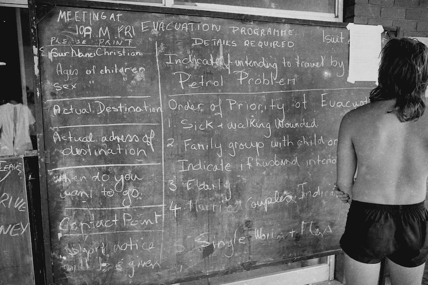 A survivor reads a blackboard showing evacuation priorities in after Cyclone Tracy struck Darwin in December 1974