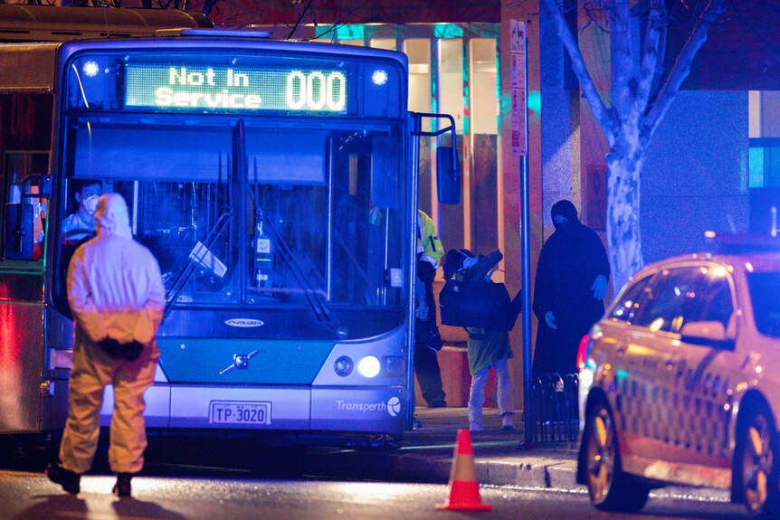 A bus outside a hotel in Perth with two Afghan women getting off the vehicle and a man wearing full PPE standing in front of it.