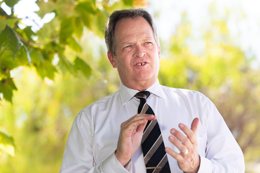 A man in a white shirt with a black and gold tie stands outside looking into the distance.