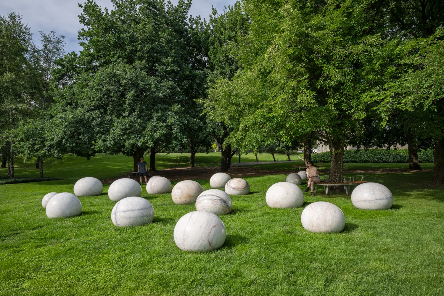 A woman sits underneath a tree surrounded by beautifully smooth, round marble stones. 