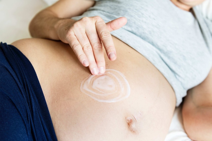 Close up of a woman's hand rubbing cream into her pregnant belly.