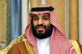 Saudi Arabia's Crown Prince Mohammed bin Salman sits next to a Saudi flag wearing a keffiyeh.
