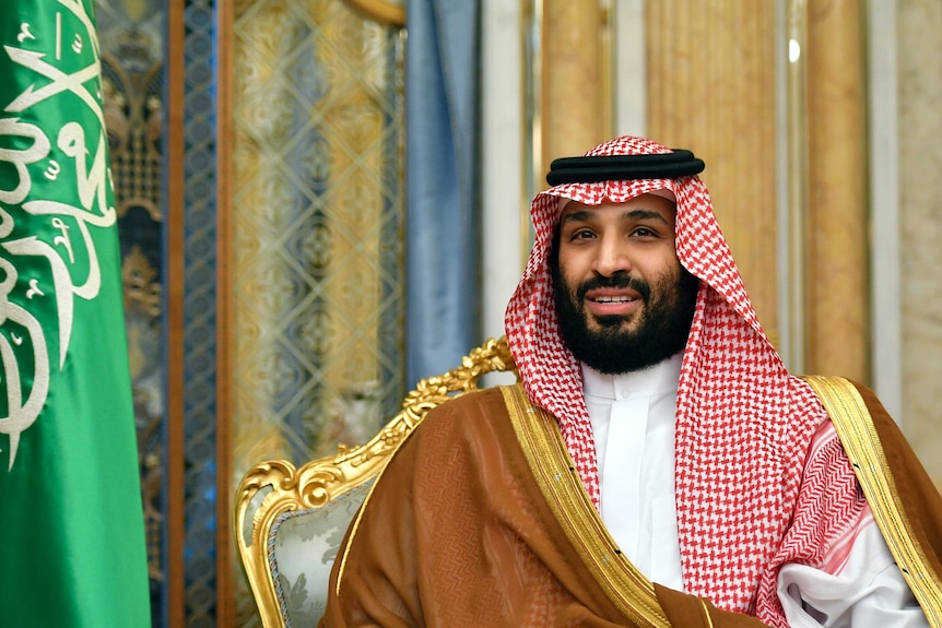 Saudi Arabia's Crown Prince Mohammed bin Salman sits next to a Saudi flag wearing a keffiyeh.