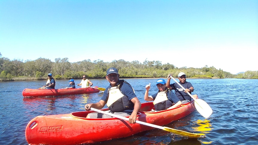 Indigenous and Indonesian people paddling three orange kayaks in an estuary