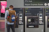 A man with his back to the camera uses one of four myki machines below a sign directing people to regional and metro trains.