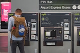 A man with his back to the camera uses one of four myki machines below a sign directing people to regional and metro trains.