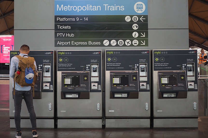 A man with his back to the camera uses one of four myki machines below a sign directing people to regional and metro trains.