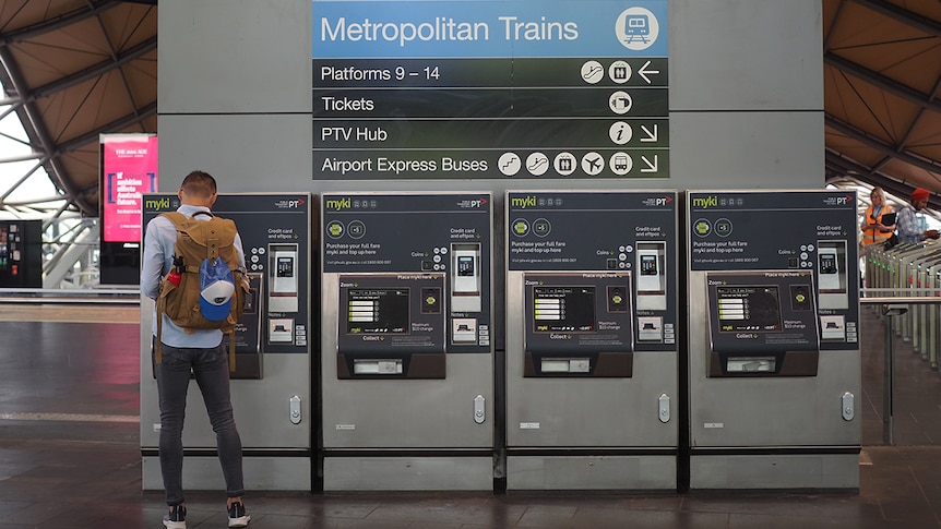 A man with his back to the camera uses one of four myki machines below a sign directing people to regional and metro trains.