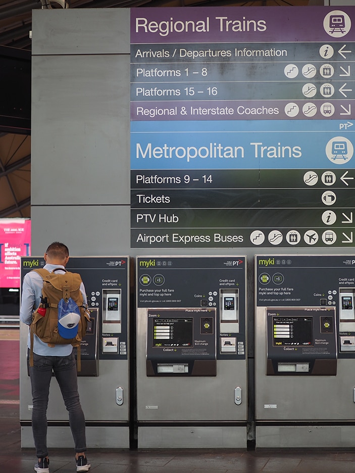 A man with his back to the camera uses one of four myki machines below a sign directing people to regional and metro trains.