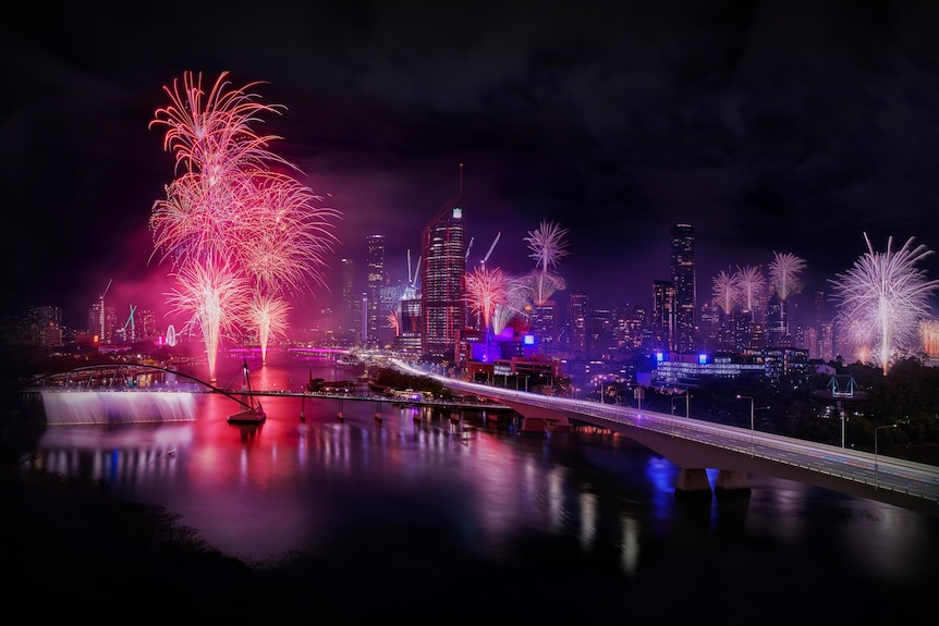 a wide shot of the brisbane cbd at night with fireworks exploding over the river