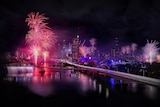 a wide shot of the brisbane cbd at night with fireworks exploding over the river