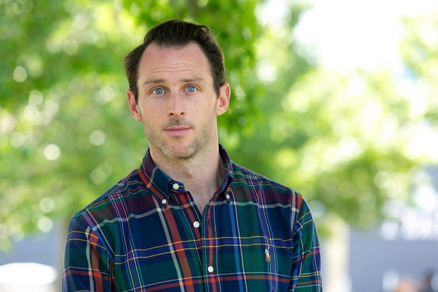 A man in a flanno shirt looking at a camera with blue eyes.