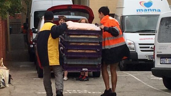 Men unload crates of hot dog buns on a driveway.