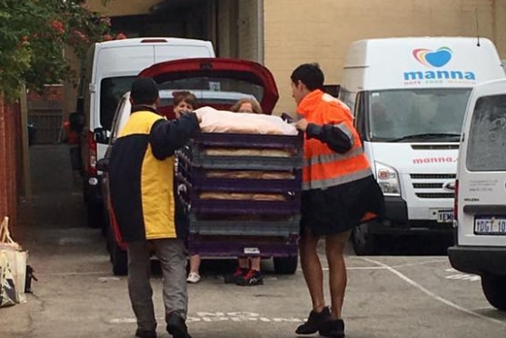 Men unload crates of hot dog buns on a driveway.