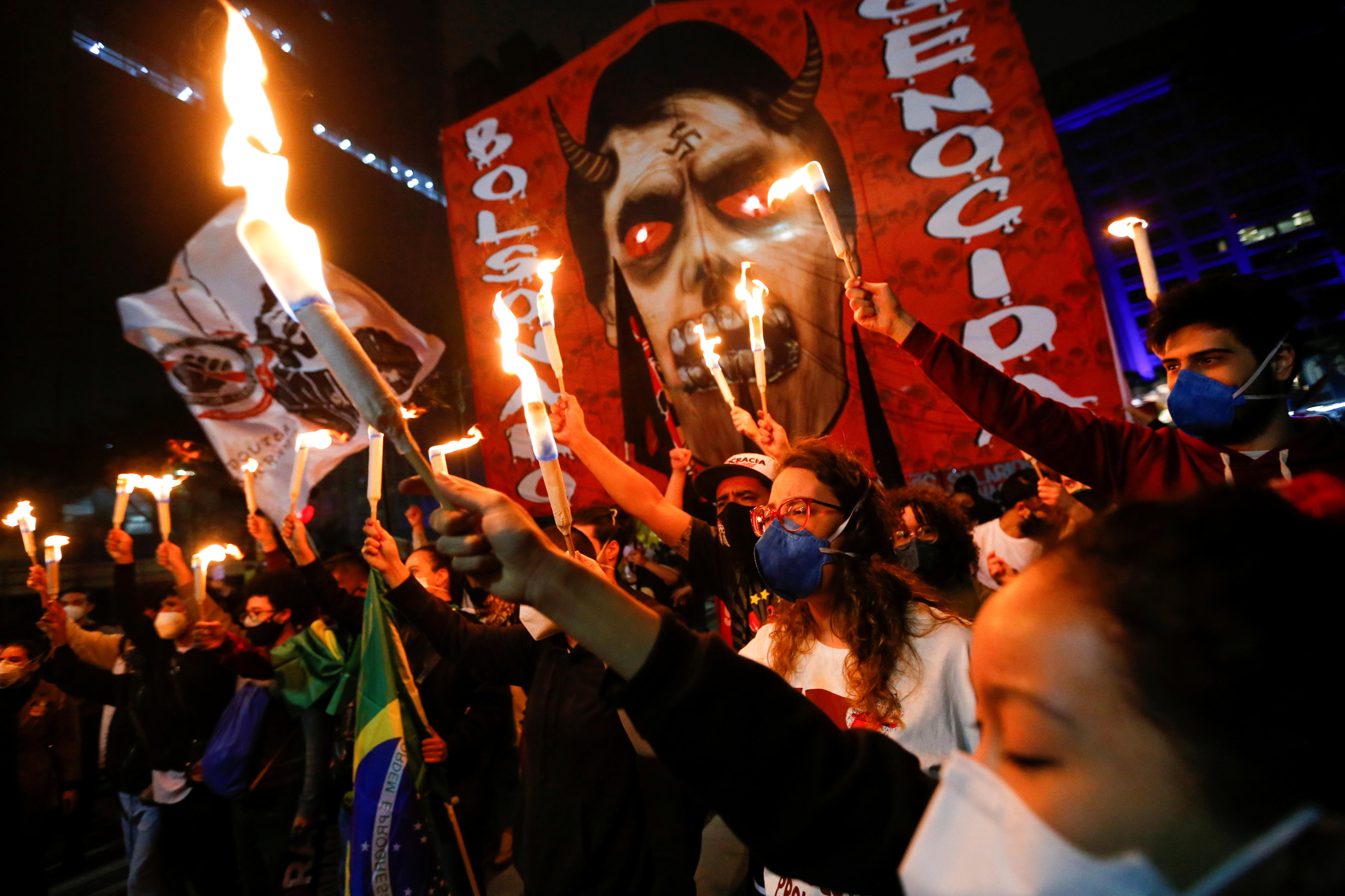 Protesters hold flames in front of a photo of Bolsonaro drawn as the devil