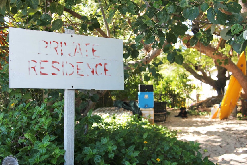 A 'private residence' sign in the sand with some marine equipment in the background.